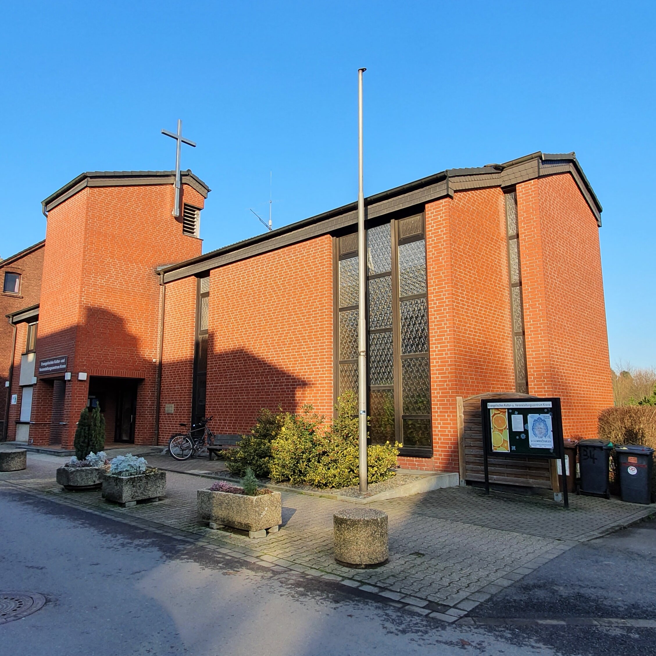 Foto: Ev. Kultur- und Veranstaltungszentrum Krone: Ein aus roten Ziegeln gemauertes zweigeschossiges Gebäude, mit einem etwa dreigeschossigem kleinen Turm, an dem ein Kreuz befestigt ist.